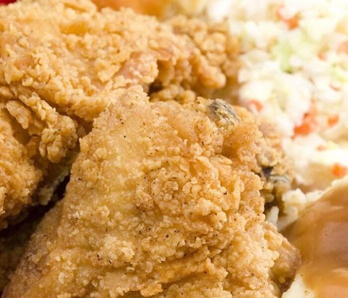 Hand-breaded fried chicken with a biscuit and coleslaw on a red plate