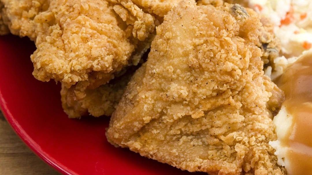Southern fried chicken on a red plate with coleslaw and mashed potatoes with gravy